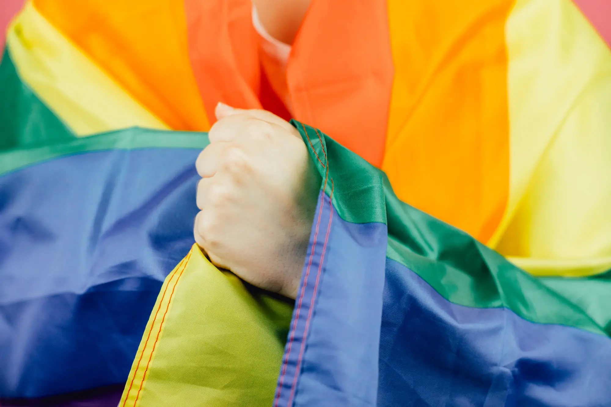 Close up hand over flag. Woman smiling happily to camera while holding a LGBTIQ