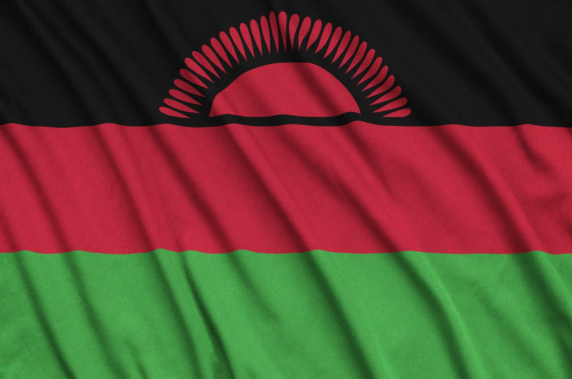Malawi flag is depicted on a sports cloth fabric with many folds. Sport team waving banner