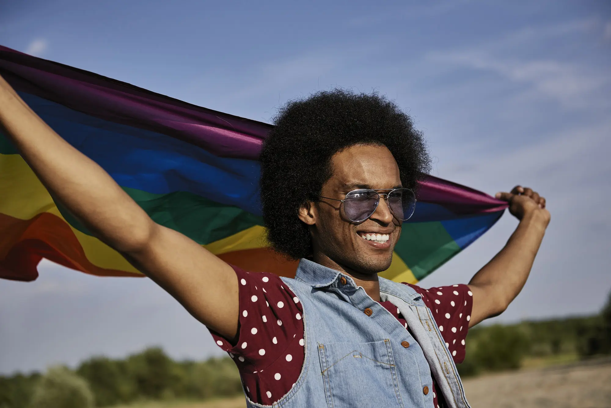 Young African man with rainbow flag standing at beach